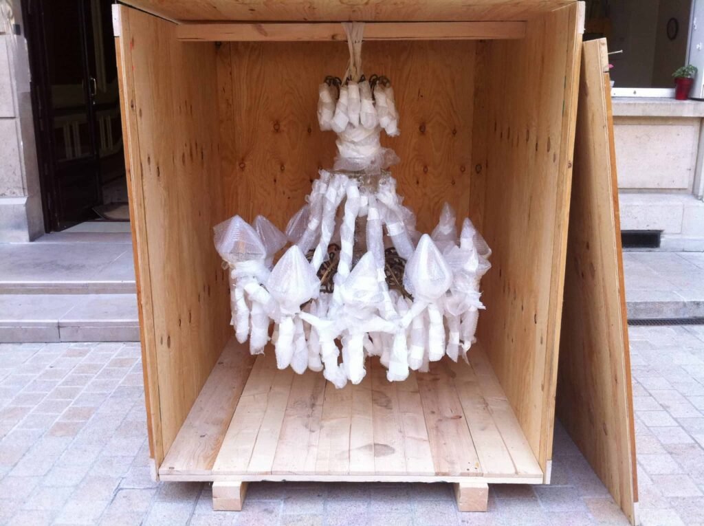 Un lustre est suspendu et emballé dans du papier bulle dans un garde meubles. La caisse est posée sur un sol prête pour un déménagement sécurisé d'objets fragiles et de valeur.