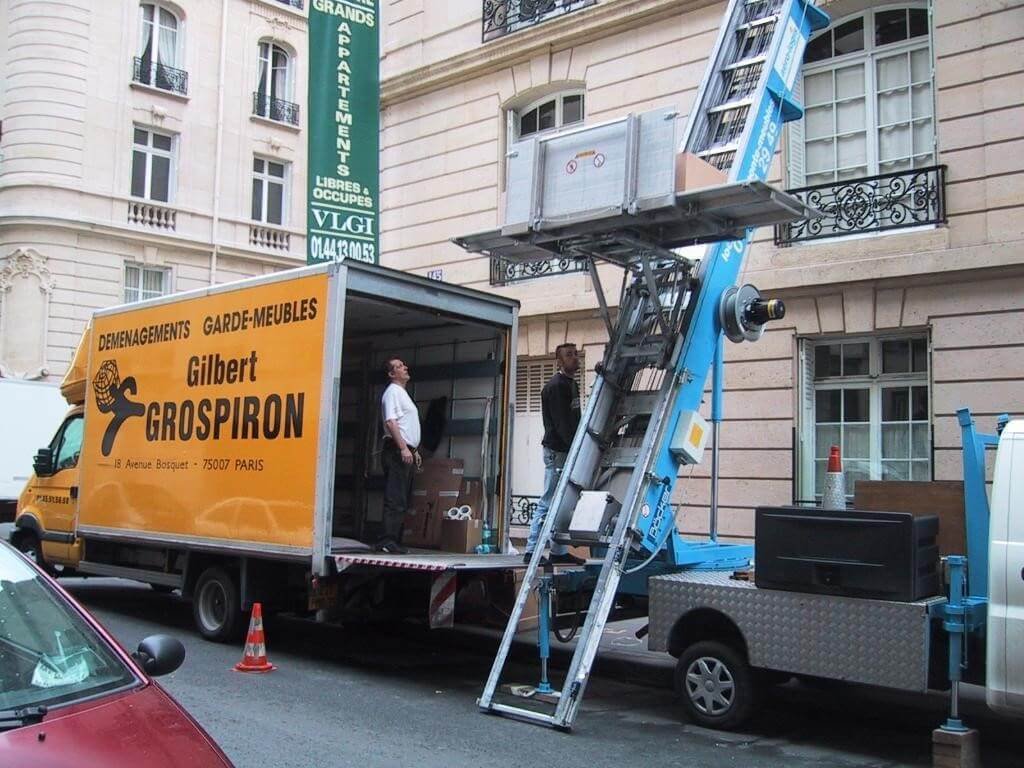 Un camion de déménagement jaune "Gilbert GROSPIRON" est garé devant un immeuble. c'est un déménagement en cours à Paris.